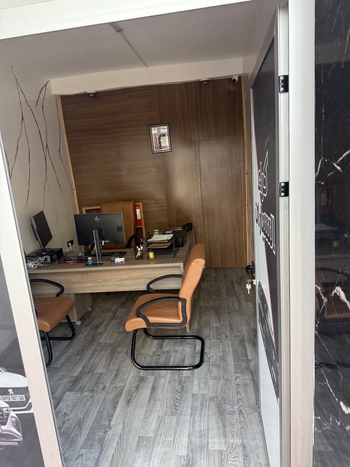 Porte vitrée ouverte de l’agence, fauteuils en cuir et bureau à l’intérieur